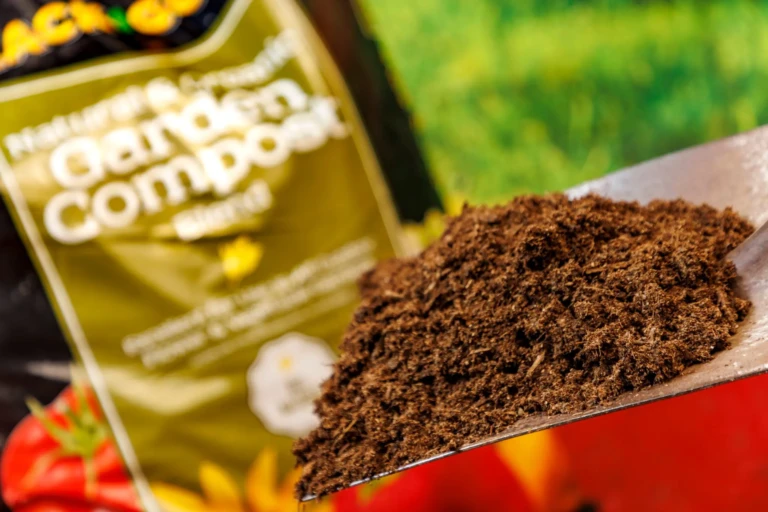 Shovel heaping of rich SunGro coir compost on a trowel with blurred SunGro packaging and tomatoes in background