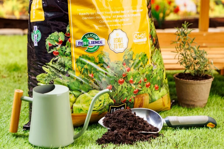 Bag of SunGro potting mix with green watering can, trowel of soil, potted herb and garden tools staged on grass